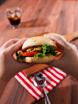 Delicious cheeseburger layer with golden bun juicy meat beef or pork patty melted cheddar cheese holding by hand on wooden background fresh ingredients lettuce tomatoes tasty classic burger junk food.