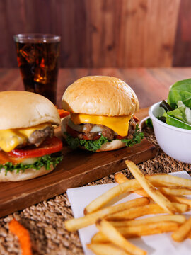 Fresh homemade cheeseburgers  juicy beef patties melted cheese lettuce tomato served on wooden board with crispy french fries creating delicious casual dining meal tasty classic fast food advertising.