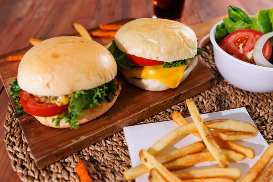 Fresh homemade cheeseburgers  juicy beef patties melted cheese lettuce tomato served on wooden board with crispy french fries creating delicious casual dining meal tasty classic fast food advertising.