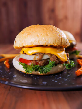 Close up of juicy cheeseburger top melted cheese beef pork patty lettuce tomato onion served with crispy french fries on black plate warm rustic background dining tasty classic fast food advertising.