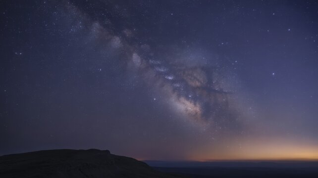 Milky way arching over dark horizon, starry night sky