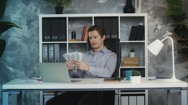 Successful young businessman counts cash and makes money rain in office