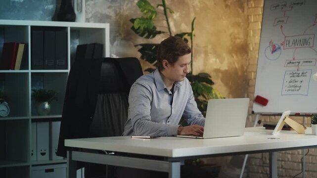 Young male company CEO closes laptop and leaves office at end of workday