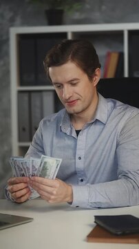 Happy businessman in his 30s counts money in office, pleased with high profit
