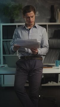 Focused male CEO reads business papers in office, checking company statistics