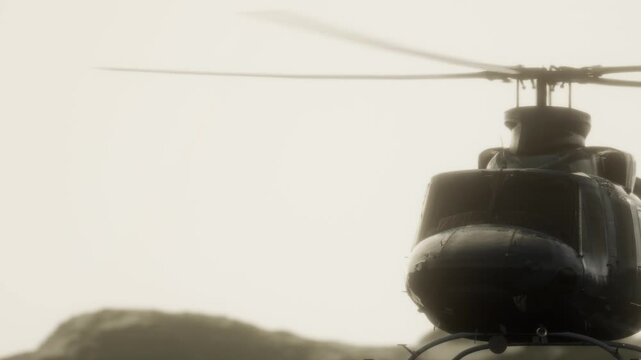 A helicopter hovers close to rugged rocks as the sun sets. The sky is brightening with colors. People may be on board or observing from the ground.