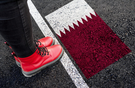 a woman with a boots standing on asphalt next to flag of Qatar and border
