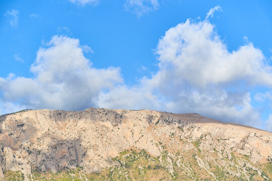 Rocky mountain summit under a blue sky with dramatic clouds, showcasing a rugged Mediterranean landscape on the island of Sicily, Italy.