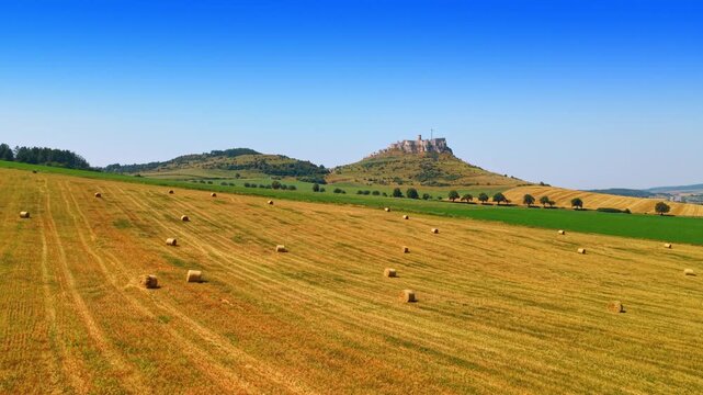 Hills with hay under bright sky. Fields of hay bales stretch across the landscape near a distant castle on a sunny day in the countryside.