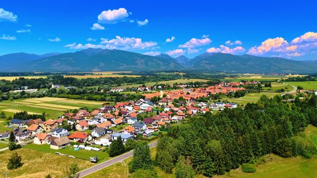Village with mountains behind. A village sits in a valley with fields and mountains around during a bright day. Houses line the streets in neat rows.