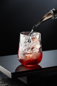 To make a Tequila Sunrise cocktail on a black table in bar.