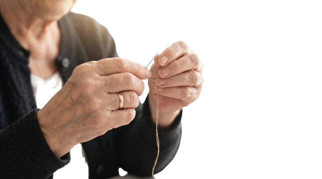 Elderly hands threading a needle, senior woman sewing with precision, close up of wrinkled hands with gold ring on white background