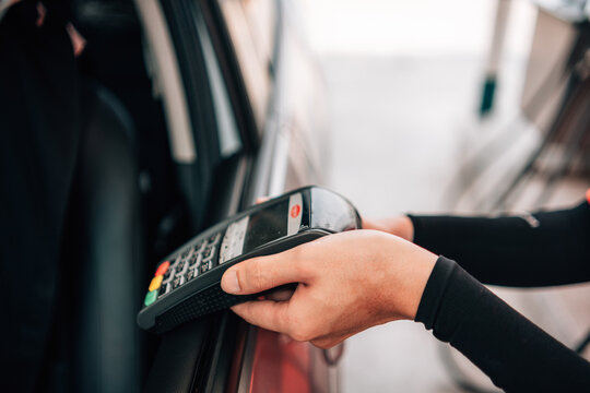 Close-up of a hand reaching out with a POS payment terminal through a car window for a drive-thru or gas station payment.