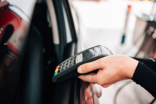 Close-up of a hand reaching out with a POS payment terminal through a car window for a drive-thru or gas station payment.