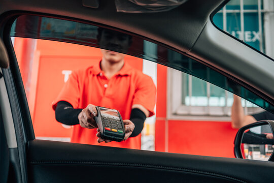 Smiling gas station attendant offering a wireless POS terminal through a car window for cashless payment.
