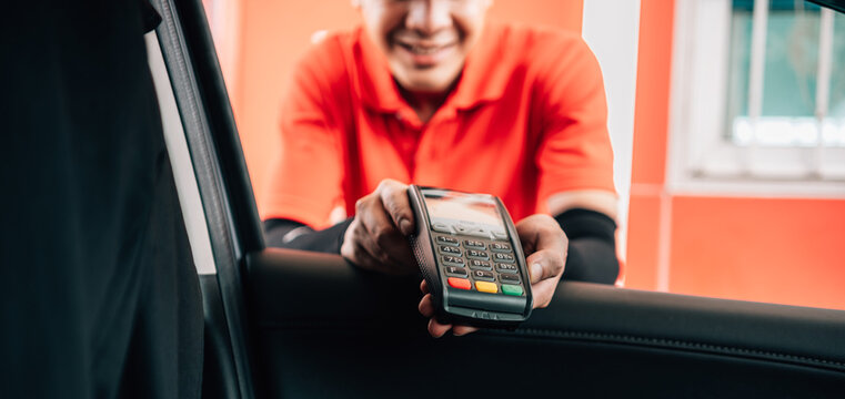 Smiling gas station attendant offering a wireless POS terminal through a car window for cashless payment.