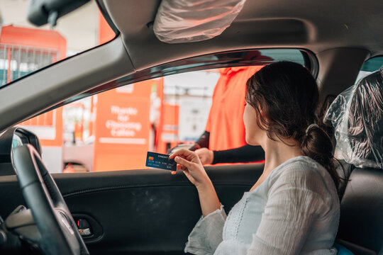 Woman making a contactless payment with a credit card terminal from her car at a gas station