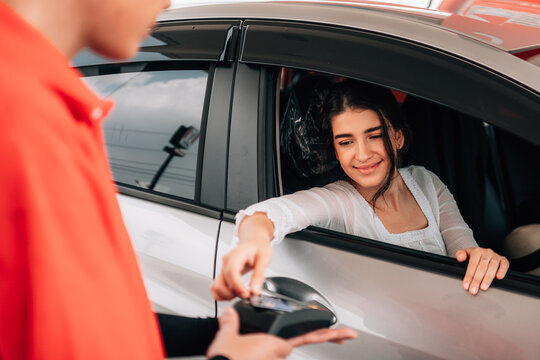 Woman making a contactless payment with a credit card terminal from her car at a gas station