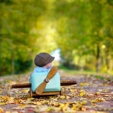 Little Boy Playing Pilot in a Wooden Airplane on an Autumn Avenue