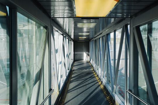 Empty airport jet bridge corridor leading toward aircraft boarding area. Glass walls and metal framework form aviation travel background. Passenger walkway for departure and arrival gates.