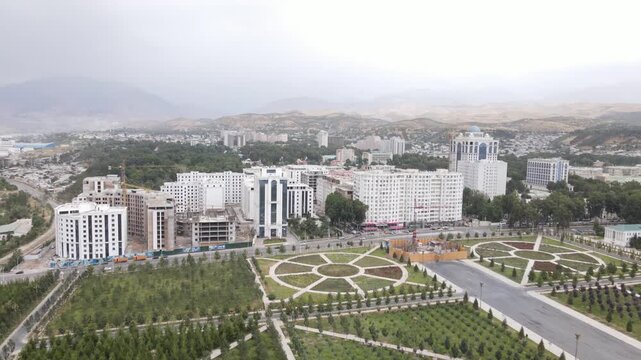 Aerial drone view over a park in Dushanbe, Tajikistan, with roads, cars, city buildings and mountains in the background