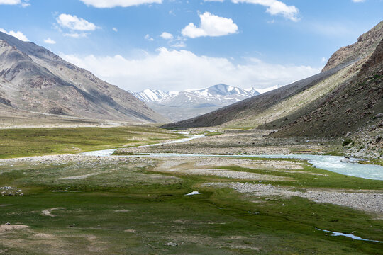 Pamir highway in Tajikistan. Mountain valley with river winding through green meadow under blue sky
