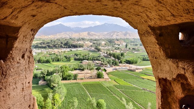 Bamiyan Buddha cliffs valley in Afghanistan. View of green farmland and distant mountains framed by ancient stone arch