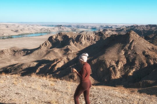 Side profile of a female hiker with a mug looking out over the winding Ili River canyon in Kazakhstan, suitable for tourism marketing, adventure lifestyle banners, and outdoor recreation.