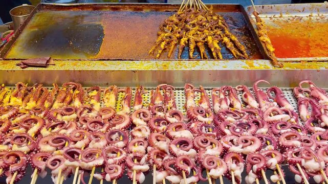 Korean Street Food &ndash; Grilling Octopus Skewers on Hot Griddle with Spicy Glaze at Night Market Stall