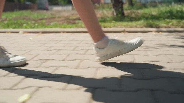 Close up of person legs and white sneakers walking on paved ground with green grass background. continuous movement shows feet in various positions during steps capturing texture detail