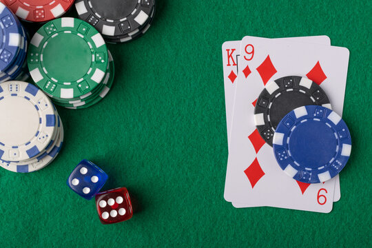 Close up top view of casino poker chips, pair of playing cards, and two dice resting on green felt table background.