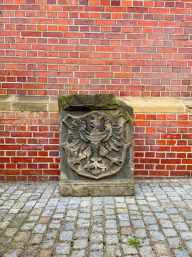 Ancient stone heraldic coat of arms with double-headed eagle carved relief leaning against weathered red brick wall on cobblestone street
