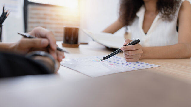 A young businessman and a businesswoman discussing work over a financial report and charts in an office.