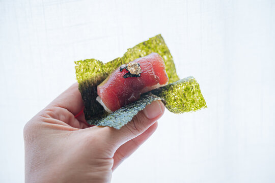 Close up of person holding delicious fresh maguro tuna sushi nori wrap fine dining omakase style.