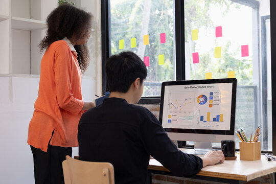 Two diverse colleagues collaborating in a modern office, analyzing sale performance charts and financial data on a computer screen.
