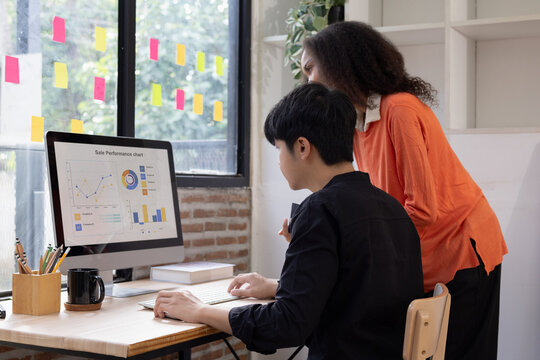 Two diverse colleagues collaborating in a modern office, analyzing sale performance charts and financial data on a computer screen.
