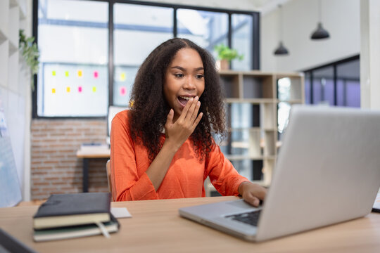 A cheerful young African American woman celebrating success while working on a laptop at her office desk.