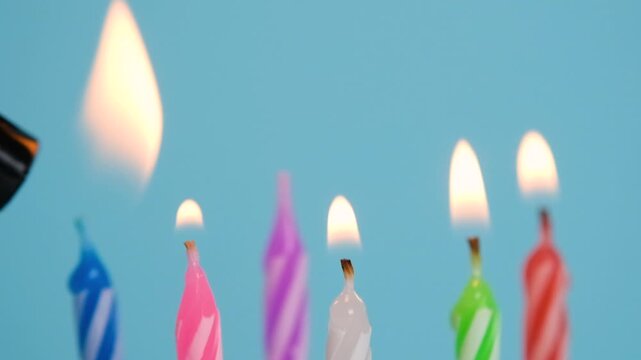Birthday candles being lit with a lighter and burning with a bright flame against a soft blue background.
