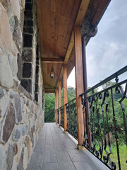 Naklejka premium Covered wooden balcony with a stone wall and ornate metal railing overlooking greenery