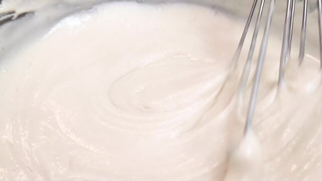 Mixing thick, white, creamy batter with a metal whisk in a bowl during the homemade cooking process