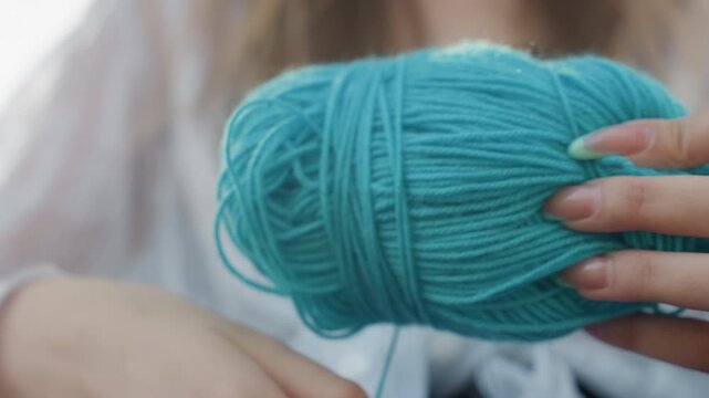 Close up of woman holding turquoise yarn preparing to crochet with soft lighting and natural nail polish. focus remains on hands manipulating thick thread emphasizing texture detail