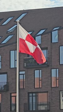 National flag of Greenland, known as Erfalasorput, waving majestically against a modern brick building, symbolizing national pride, arctic territory, and the Denmark USA political dispute