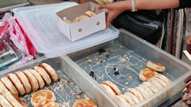 Street vendor packing fresh baked bakpia pastries into cardboard box using metal tongs