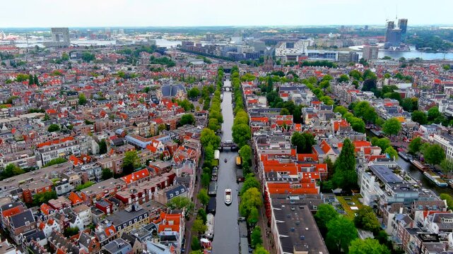 Aerial drone view of the Prinsengracht canal in Amsterdam with tour boats, the Noorderkerk church, Jordaan rooftops and the IJ harbor waterfront, Netherlands, in summer.