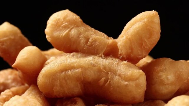 Pile of fried dough sticks or chinese cruller rotating on a black background, snack and vegan food.