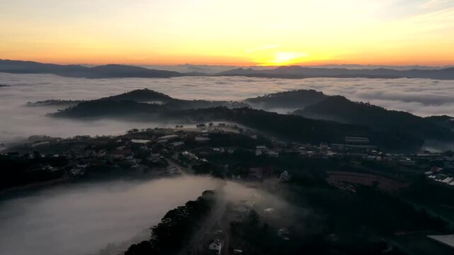Aerial sunrise over Trai Mat, Xuan Truong Ward, Da Lat, Lam Dong, Vietnam, with drifting mist, clouds and golden sunlight illuminating the peaceful highland landscape.