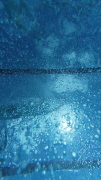 Underwater view of swimmers silhouettes and air bubbles in pool