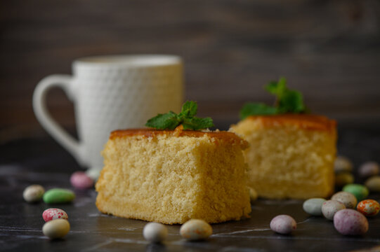 Fresh homemade sponge cake pieces with mint garnish and colorful candy dragees on a dark surface
