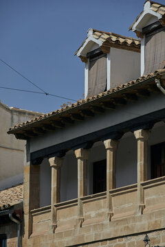 Traditional stone balcony with slender columns, timber eaves and tiled dormer windows on a historic building in Baeza, Andalusia, Spain