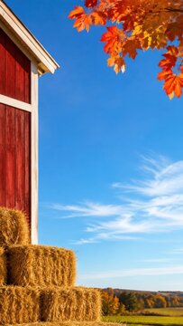 Red barn with stacked hay bales under a clear blue sky, surrounded by vibrant autumn foliage, creating a picturesque Thanksgiving Day card background